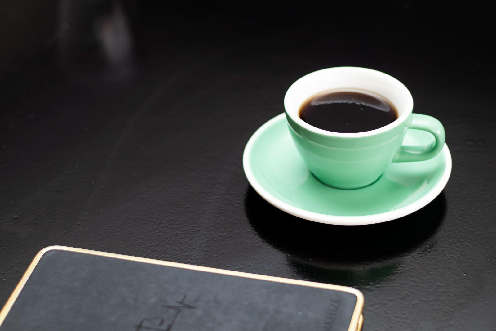 A green coffee cup and notebook on a dark table